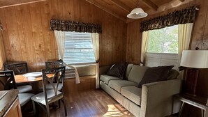A cozy cabin interior with a wooden dining table, chairs, a sofa, and a lamp. - Indian Flat RV Park - Tent Cabins & Cottages (El Portal)