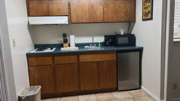 A compact kitchen with wooden cabinets, a microwave, a sink, and a trash bin.