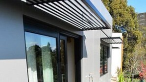A modern outdoor patio with glass doors, a round table, and wicker chairs. - Melrose Apartments (North Melbourne)