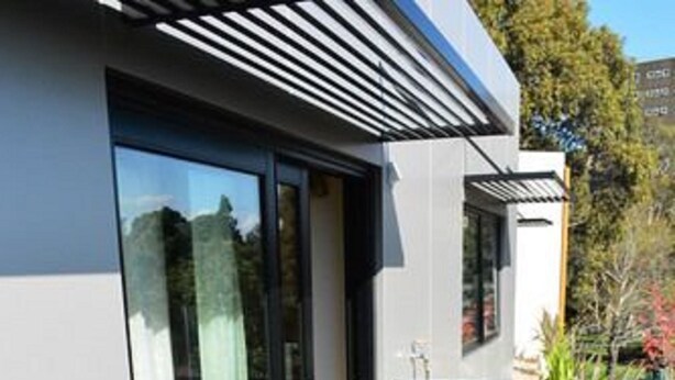 Un patio exterior moderno con puertas de vidrio, una mesa redonda y sillas de mimbre.