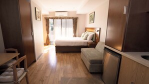 Una habitación de hotel compacta con cama, sofá, mesa de comedor y zona de cocina.