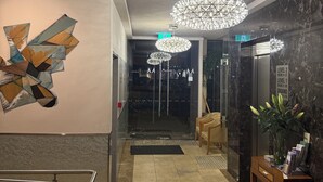 Un vestíbulo moderno con una instalación artística geométrica, un mostrador de recepción, una planta e indicaciones de niveles y números de habitación.