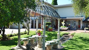 Un jardín con un pabellón, bancos de piedra y plantas en macetas.