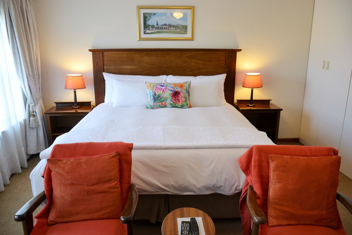 A hotel room with a large bed, two bedside lamps, a framed picture on the wall, and two red chairs.