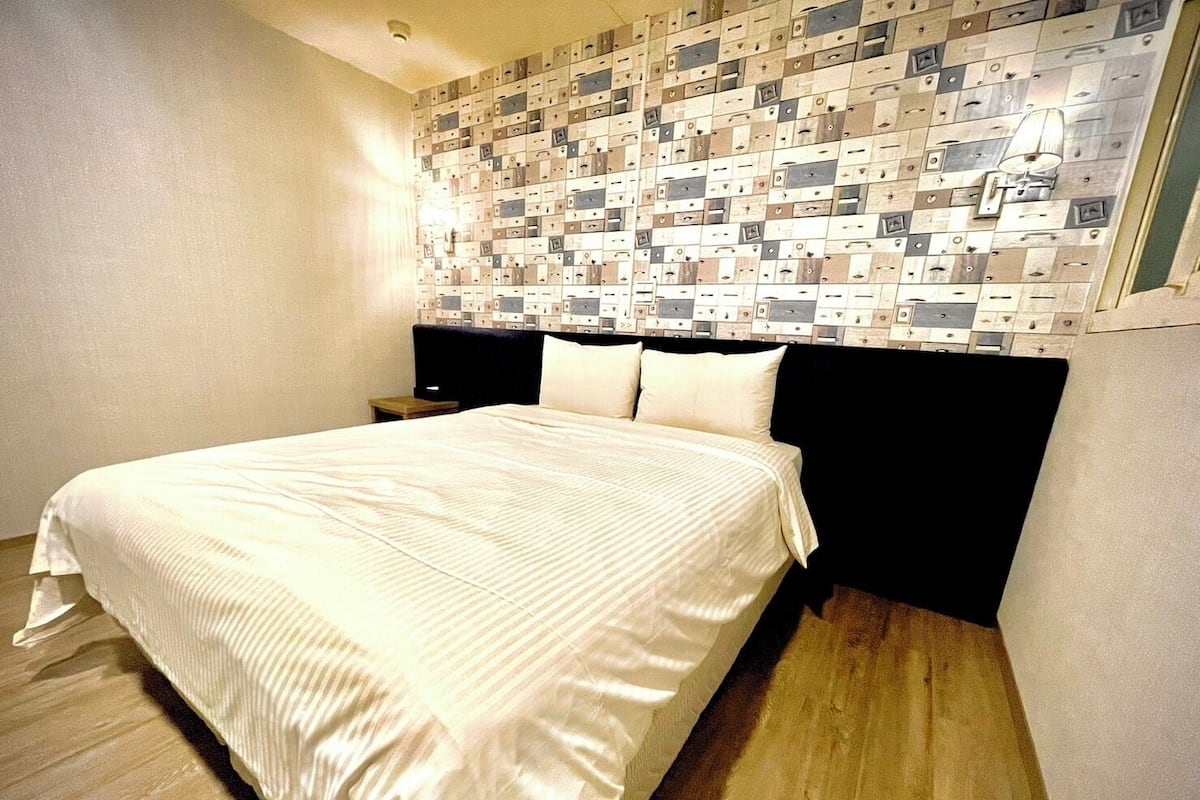 Ein Hotelzimmer mit einem ordentlich bezogenen Bett, einem Kopfteil mit einem gemusterten Design und einem Nachttisch mit einer Lampe.