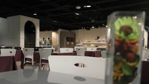 A restaurant with white tables and chairs, a kitchen area, and a glass display case with food items. - Walker Hotel - Zhengyi (New Taipei City)