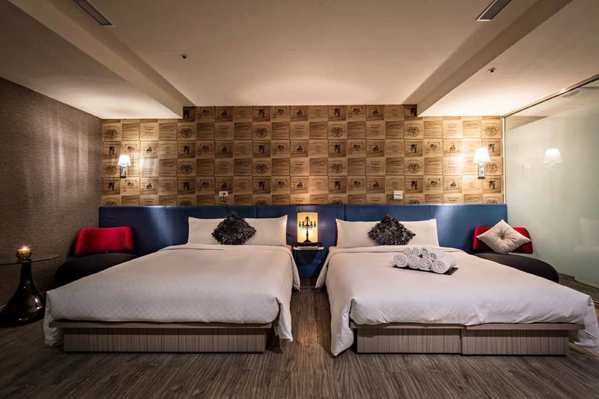 Ein Hotelzimmer mit zwei Betten, einem Kopfteil mit Plaketten, Nachttischlampen und einem Nachttisch mit Lampe.