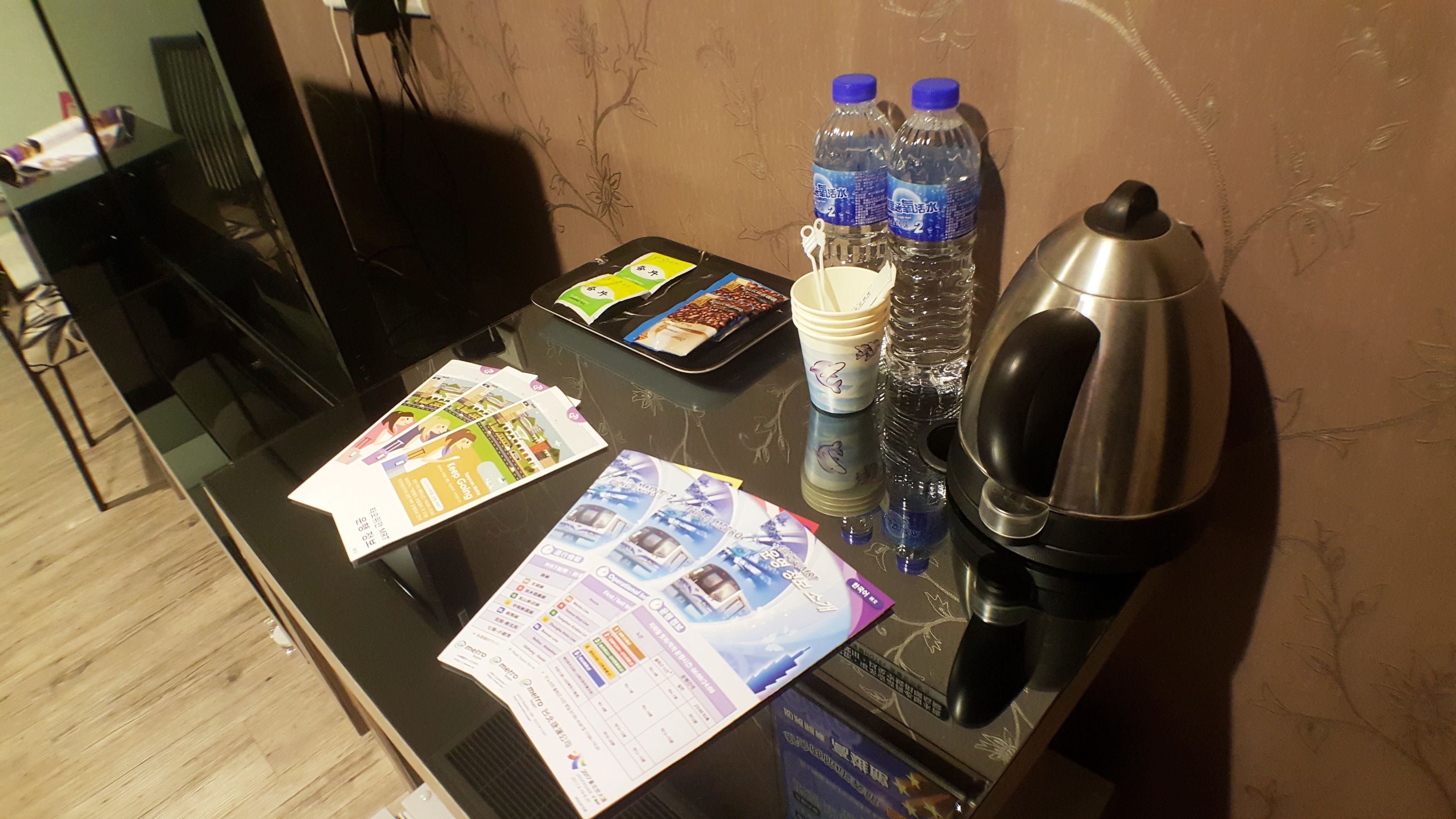 A hotel reception desk with a black surface, a kettle, two water bottles, a cup, and some informational brochures.