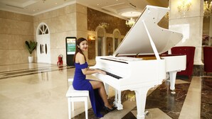 Eine Frau sitzt an einem Flügel in einer geräumigen Lobby mit Marmorboden, einem Chandelier und roten Sesseln.