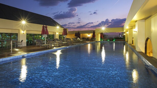 Ein großer, überdachter Pool mit Liegestühlen und Sonnenschirmen, umgeben von Wänden mit Fenstern und Beleuchtung.