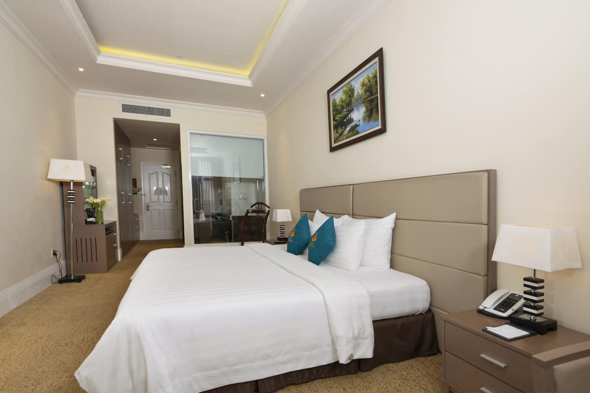 Habitación de hotel con una cama grande, lámparas de noche, una mesita de noche con un teléfono y un cuadro en la pared.