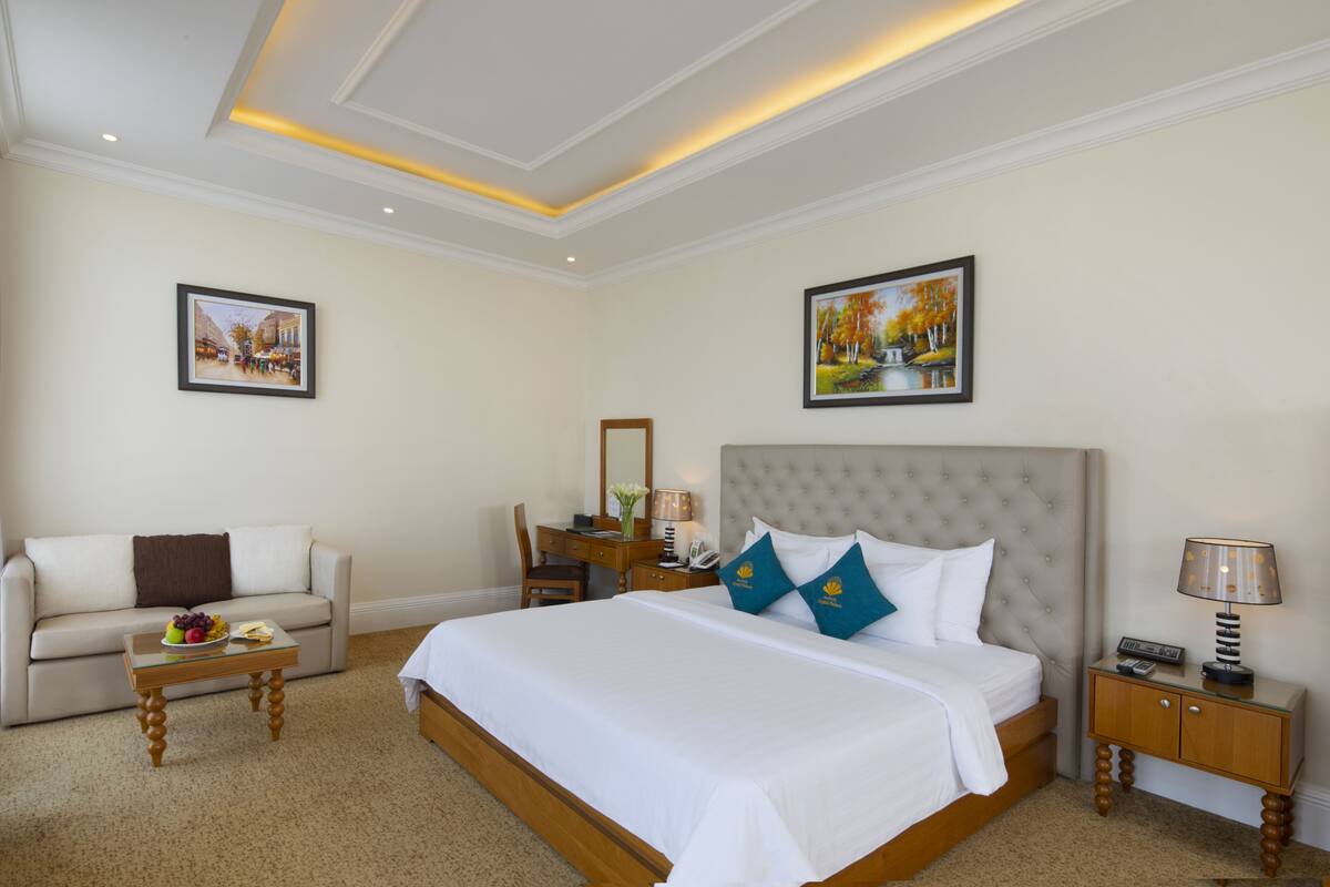 Habitación de hotel con una cama grande, un sofá, un escritorio con lámpara y dos cuadros en las paredes.