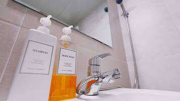 A bathroom with a sink, two bottles of shampoo and body wash, and a shower head.