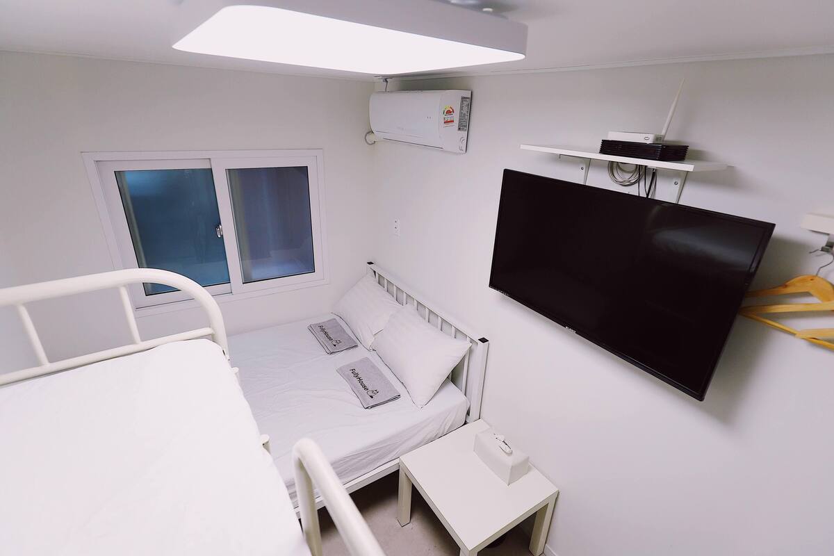 Habitación de hospital con una cama, una mesita de noche pequeña, un televisor montado en la pared y un ventanal con vidrio satinado.