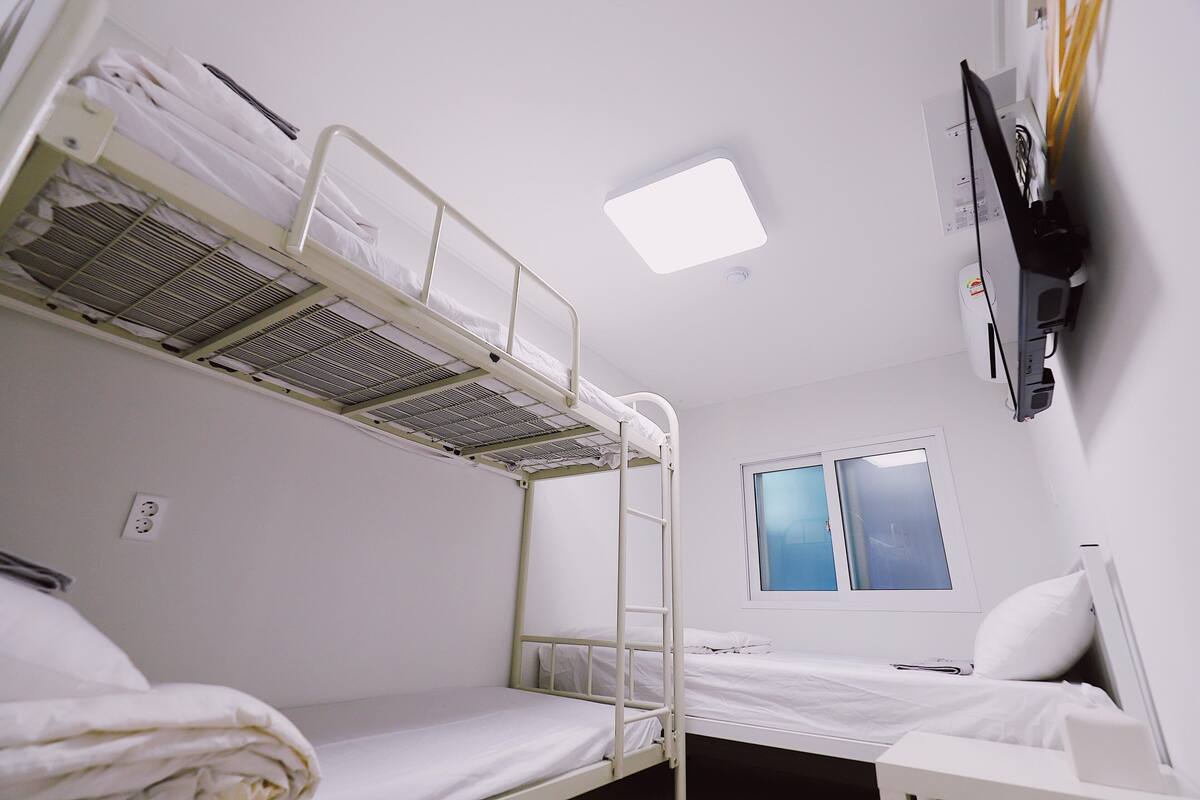 Habitación con literas, ventana, televisor de pantalla plana y toma de corriente en la pared.
