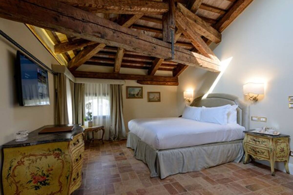 A bedroom with a bed, a dresser, a nightstand, and a ceiling with exposed wooden beams.