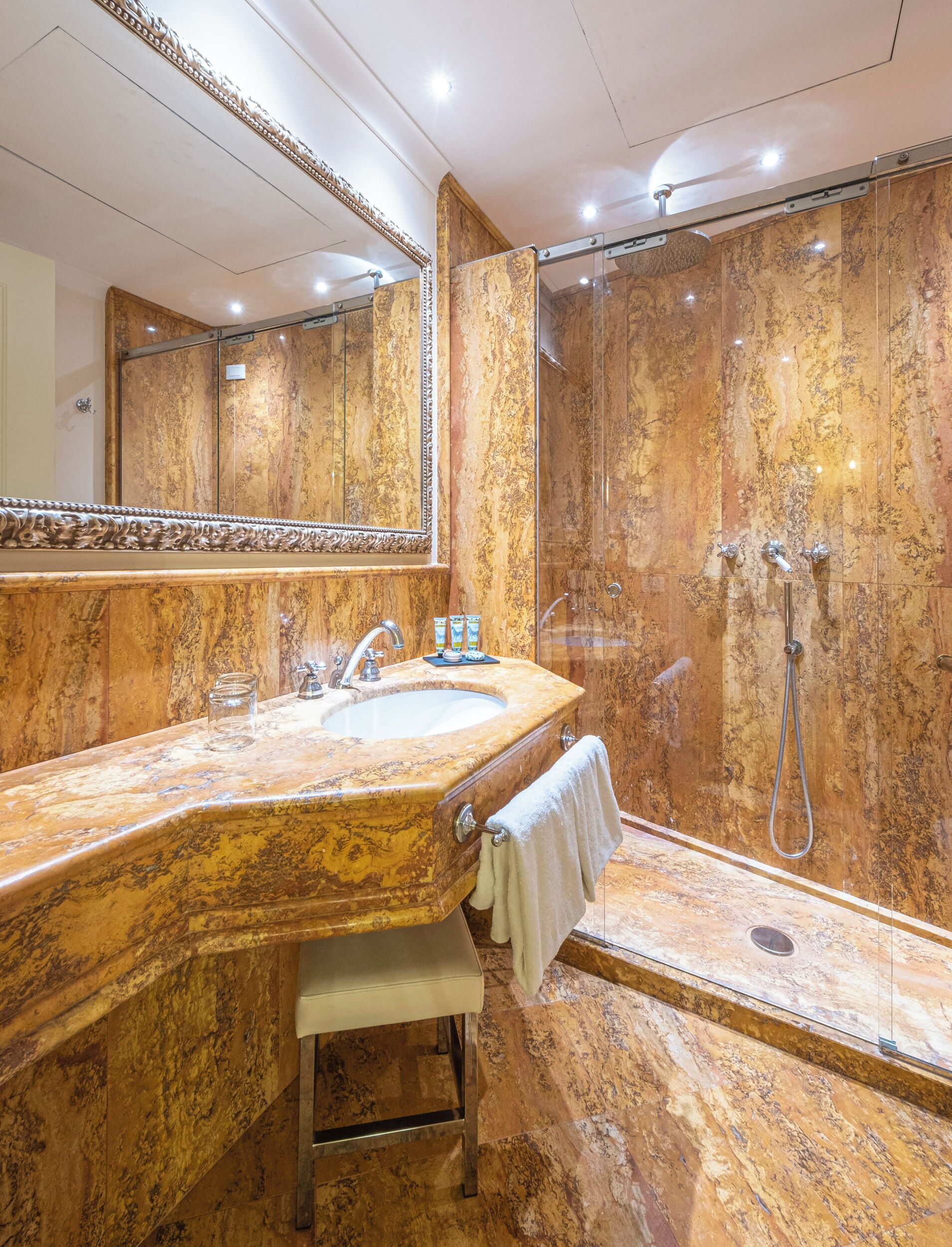 A bathroom with a marble vanity, a large mirror, a sink, and a glass-enclosed shower area.
