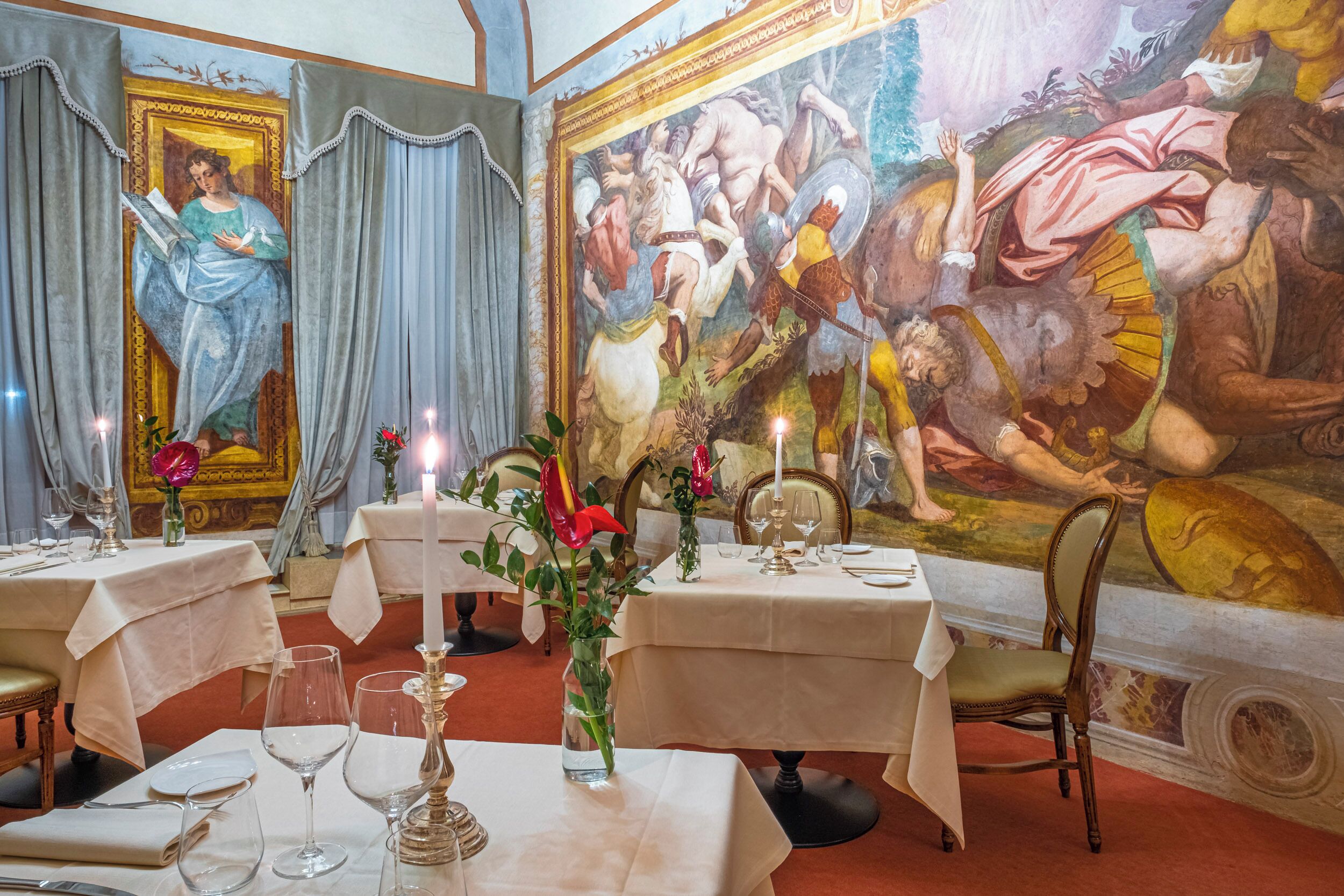 Un comedor con mesas dispuestas para el servicio, un mural grande en la pared y una araña.