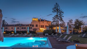 A pool area with lounge chairs and a hot tub, surrounded by a wooden deck and a building with illuminated windows. - Hotel Villa Barbarich (Mestre)