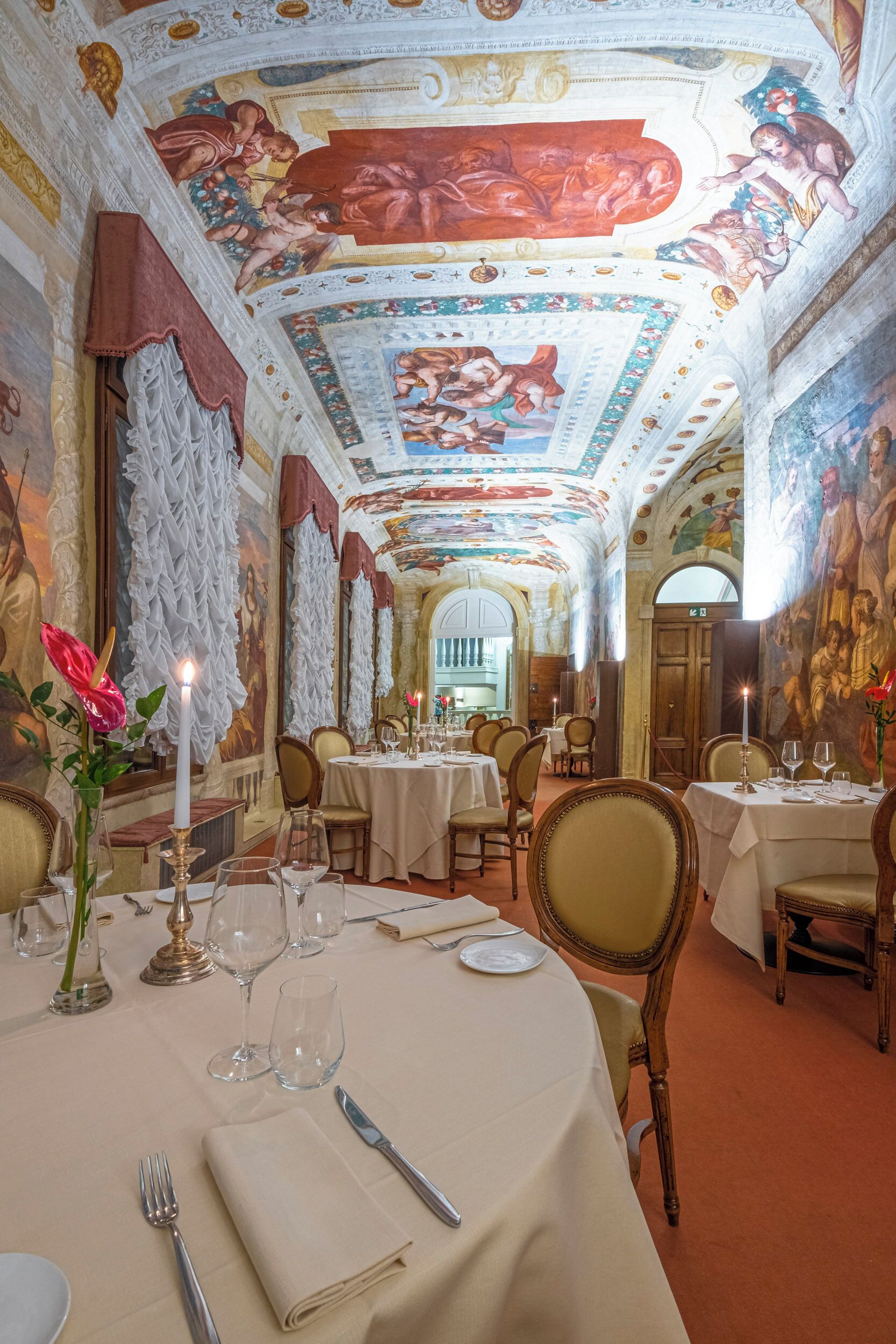 Comedor con frescos ornamentales en el techo, candelabros y decoración clásica.