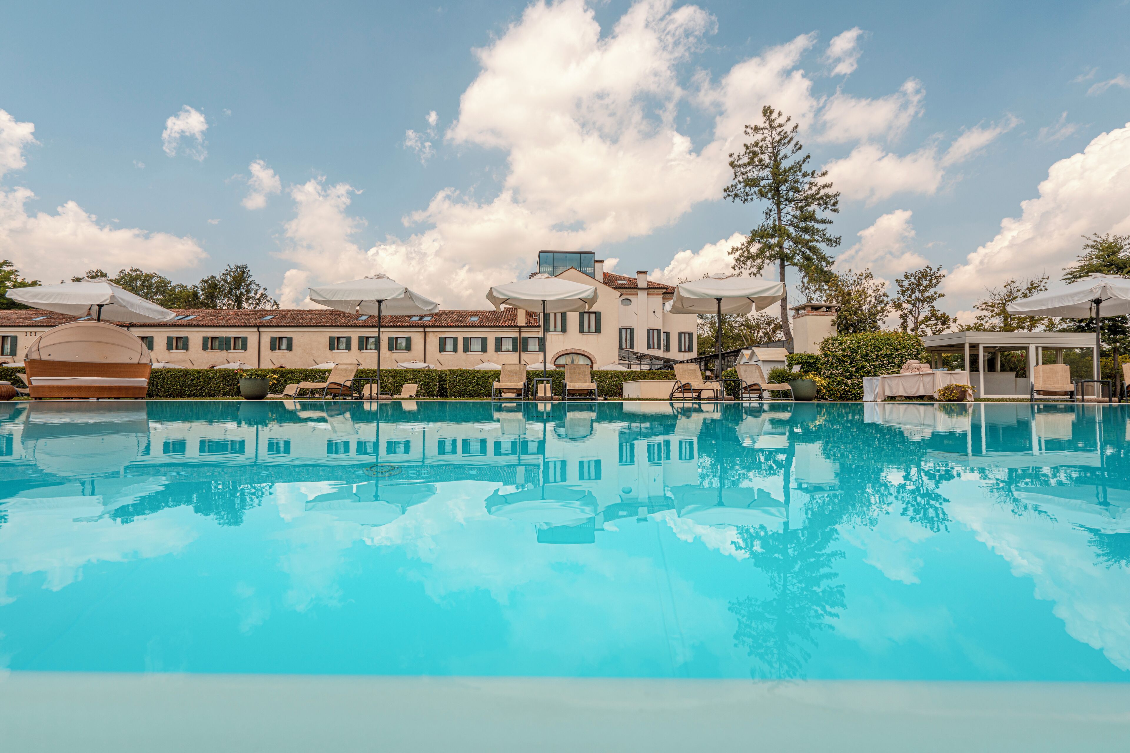 Piscina com espreguiçadeiras e guarda-sóis, cercada por edifícios sob um céu claro.