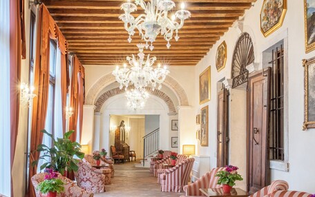 A spacious lobby with striped armchairs, a grand chandelier, and a piano.