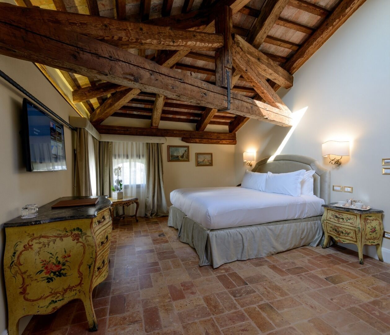 Une chambre à coucher avec un grand lit, des poutres apparentes en bois au plafond, une commode et une table de chevet avec une lampe.