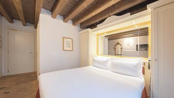 A bedroom with a large bed, a wooden ceiling, a framed picture on the wall, and a mirror with a light above it.