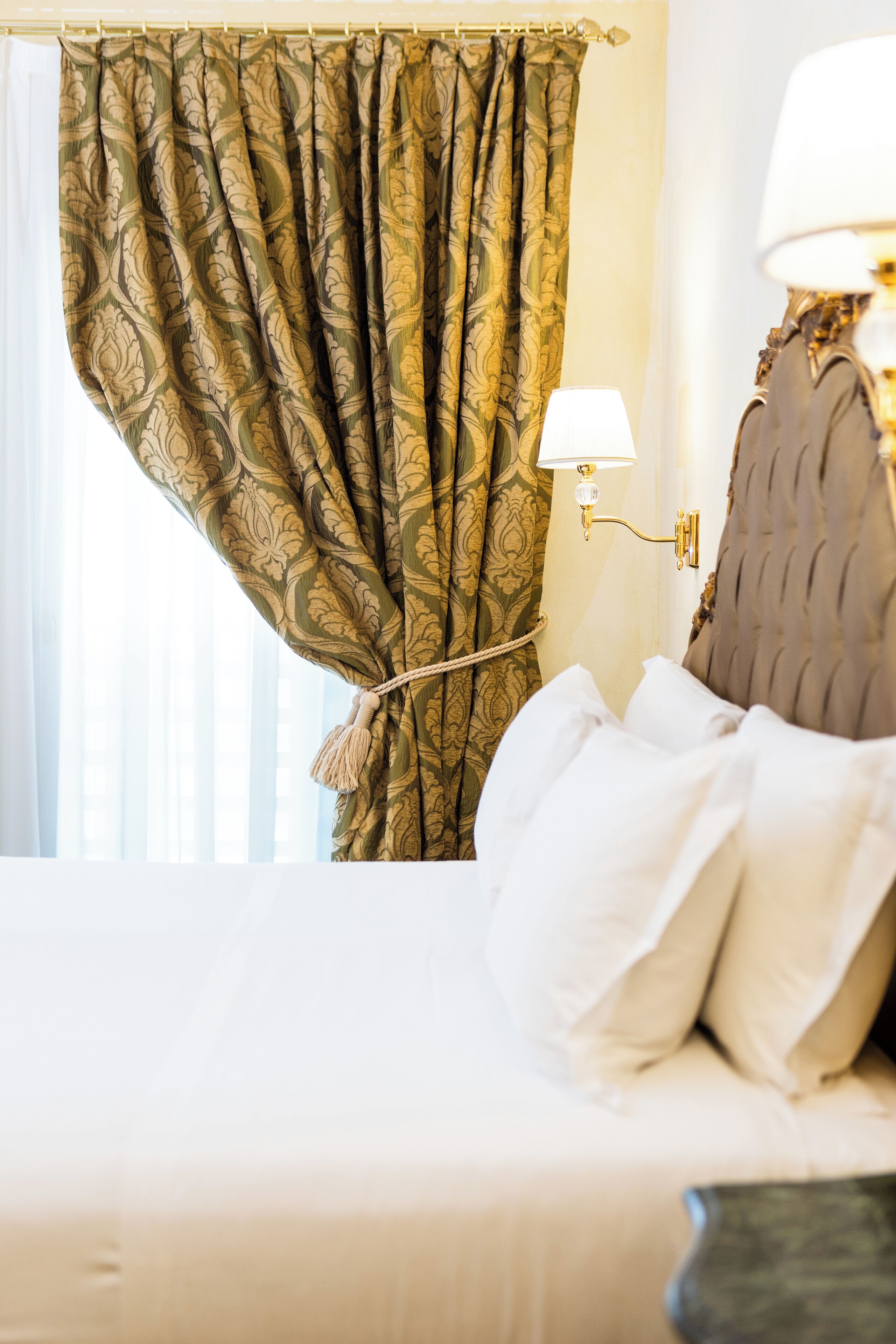 A hotel room with a bed, a nightstand with a lamp, and a window with curtains.