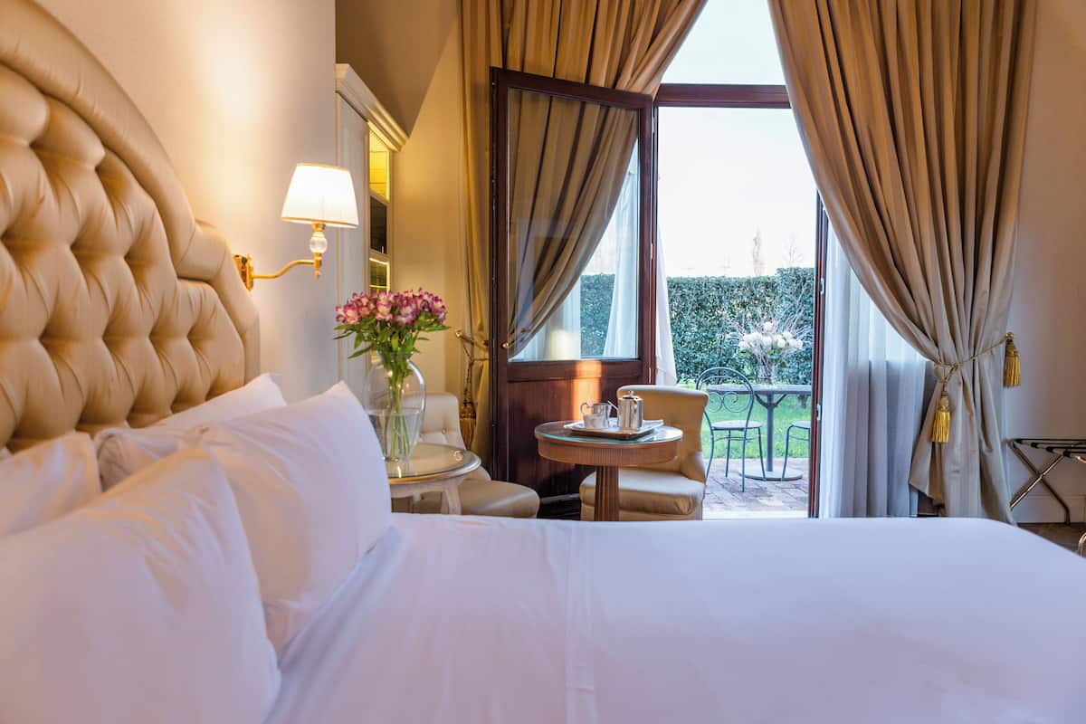 A hotel room with a large bed, a small round table with a lamp, a chair, and a view of the outdoors.
