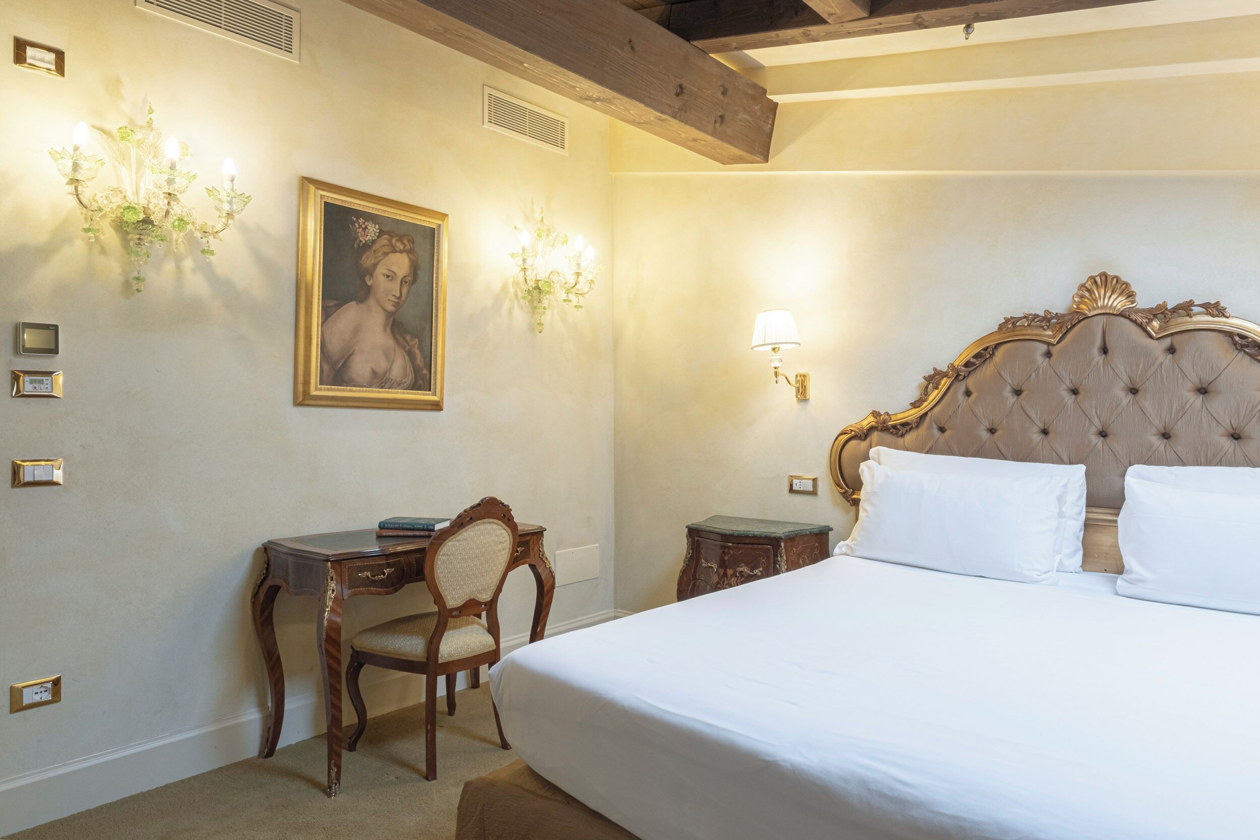 A bedroom with a large bed, a desk, a chair, and a painting on the wall.