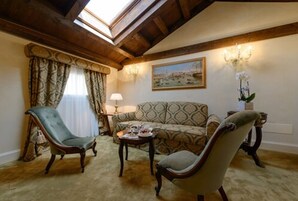 Une pièce comprenant un canapé à motifs, deux fauteuils, une petite table avec un plateau, un tableau au mur et un lustre.