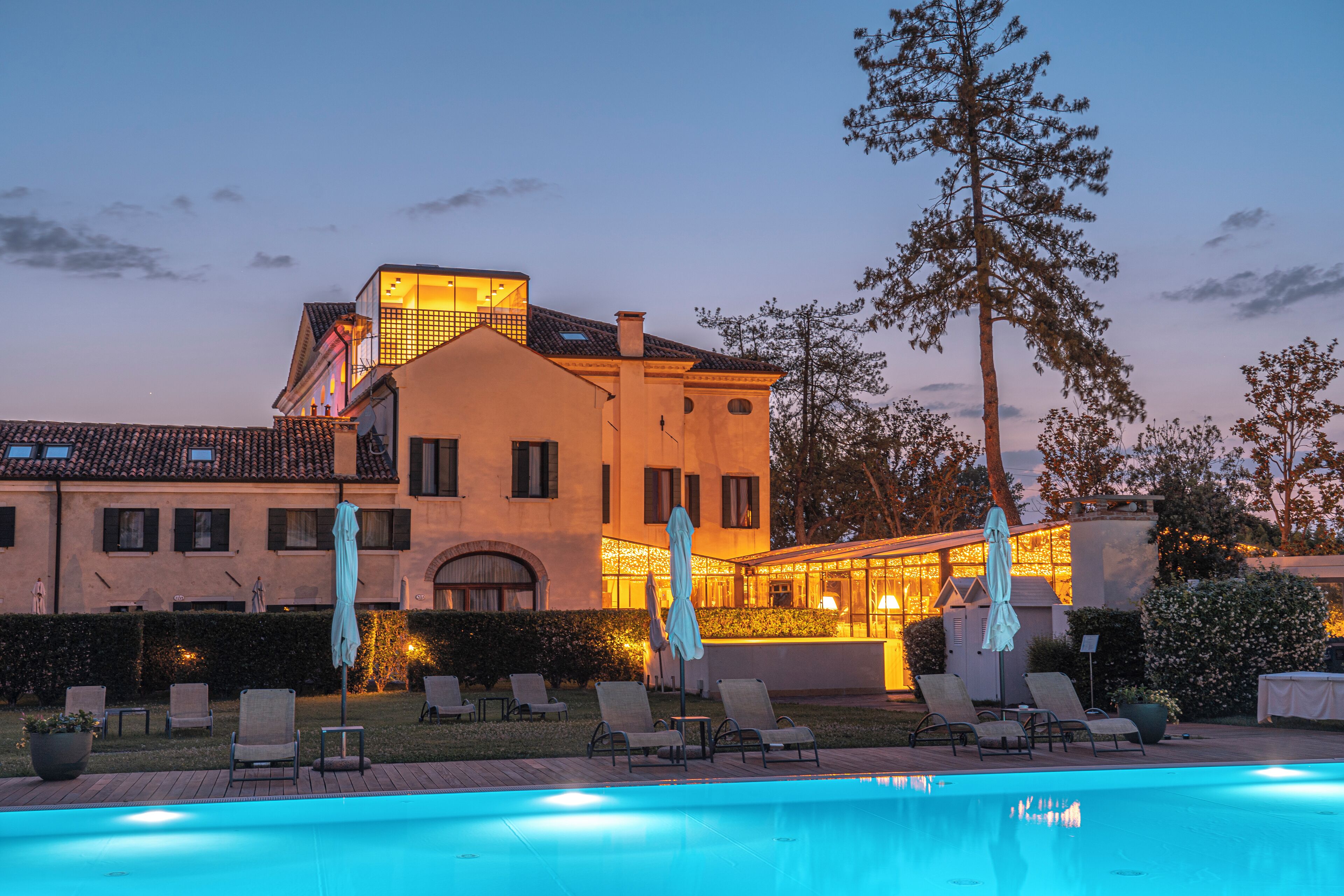 A large building with a swimming pool, outdoor seating, and a well-lit facade.