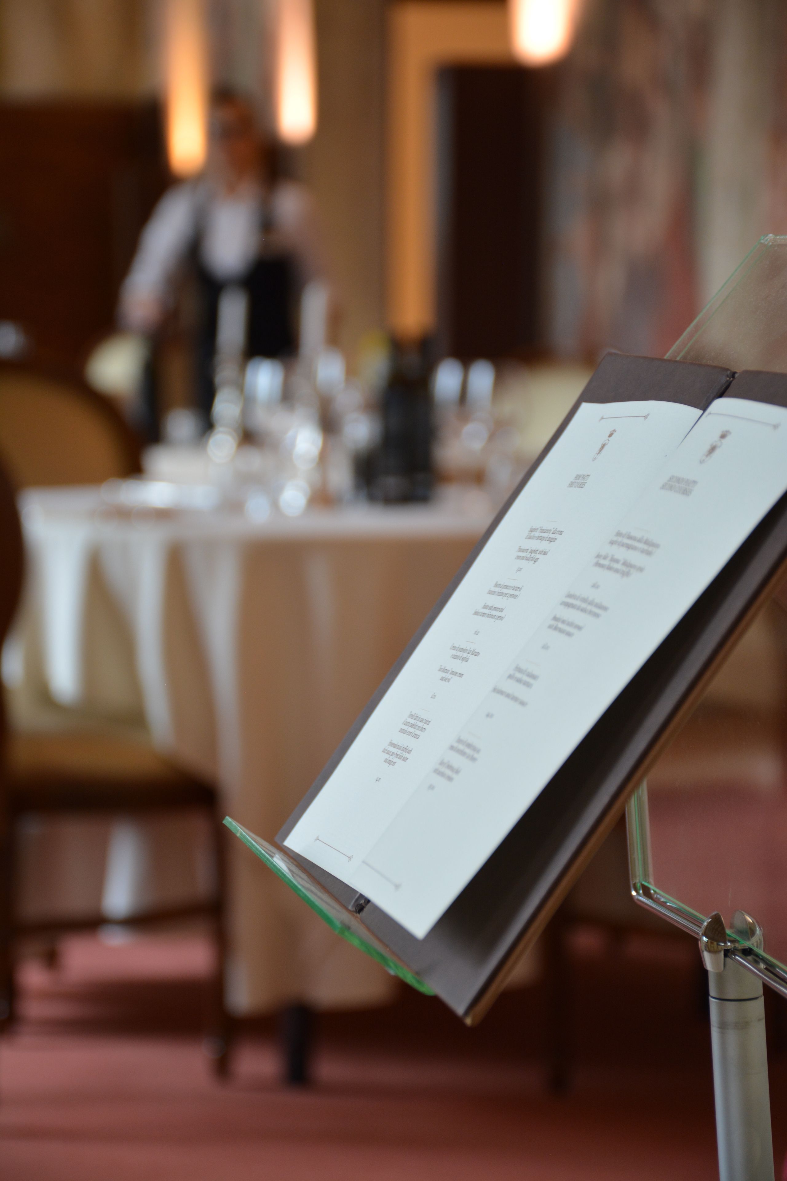 Ein Speisekartenständer in einem Restaurant, im Hintergrund verschwommen ein Esstisch mit Stühlen.