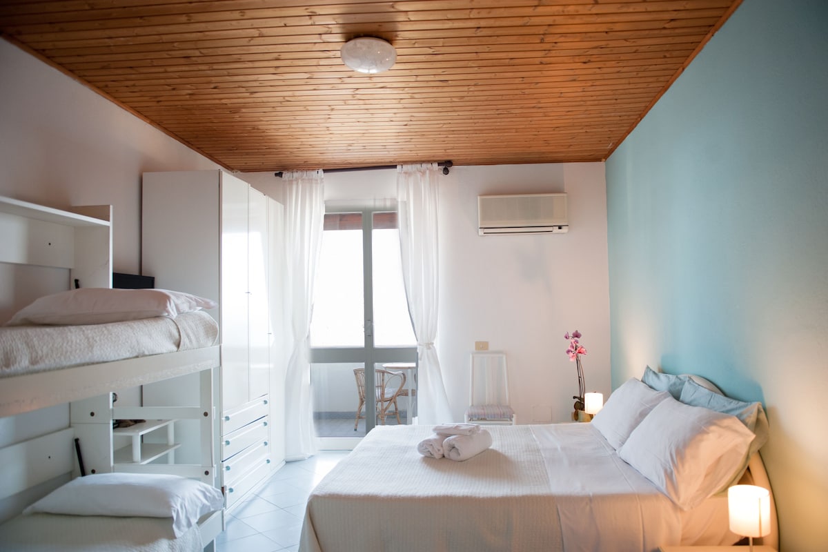 A bedroom with bunk beds, a bed with pillows, a chair, and a nightstand with a lamp.