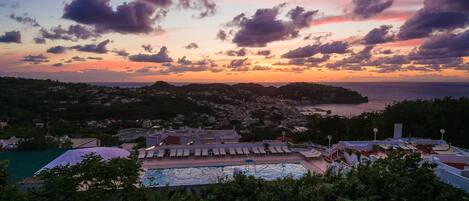 Un resort con piscina, sillones de descanso y vistas al mar y al pueblo al atardecer.