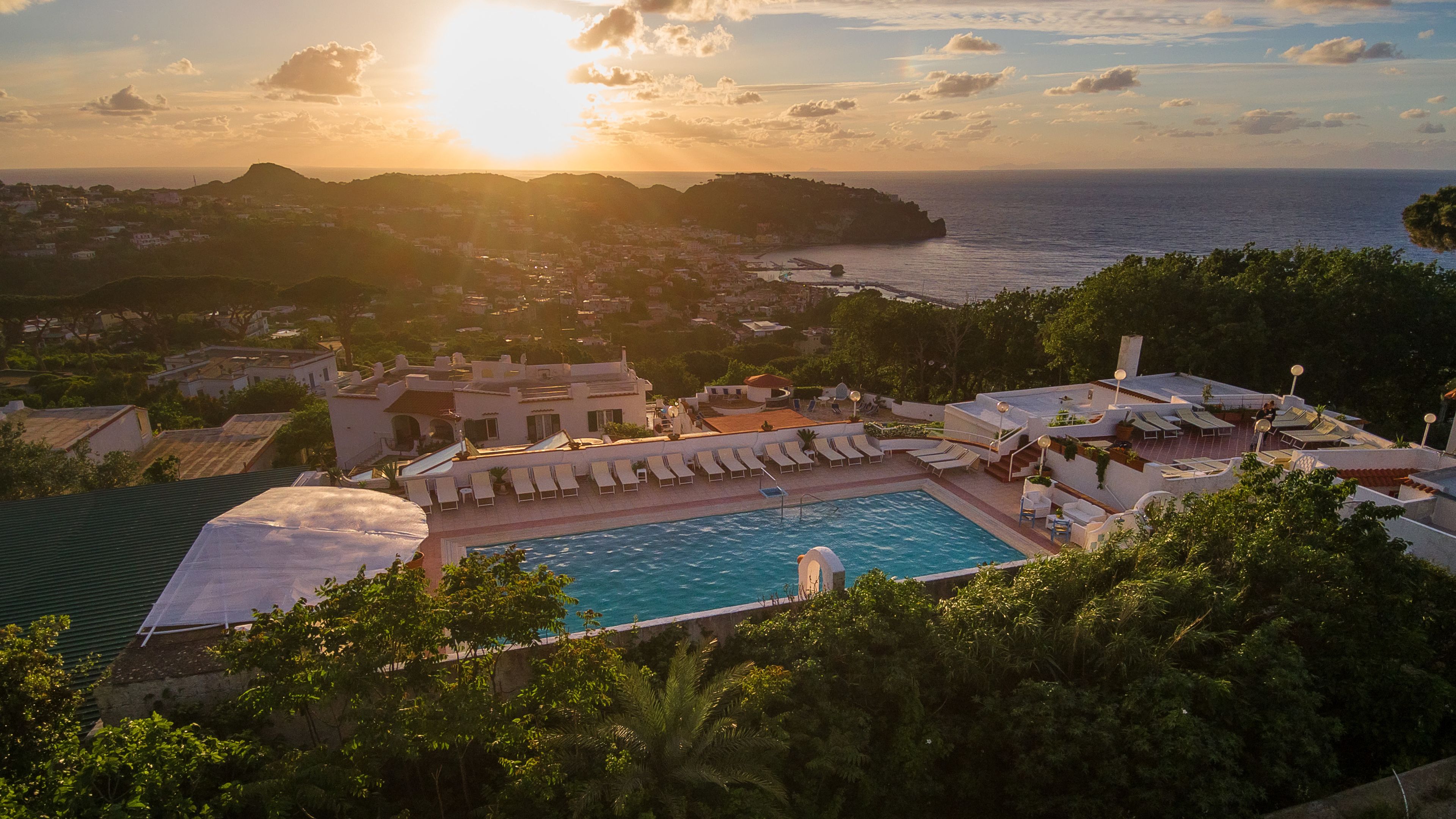 Un complexe hôtelier doté d’une piscine, de chaises longues et offrant une vue sur la mer et les collines.