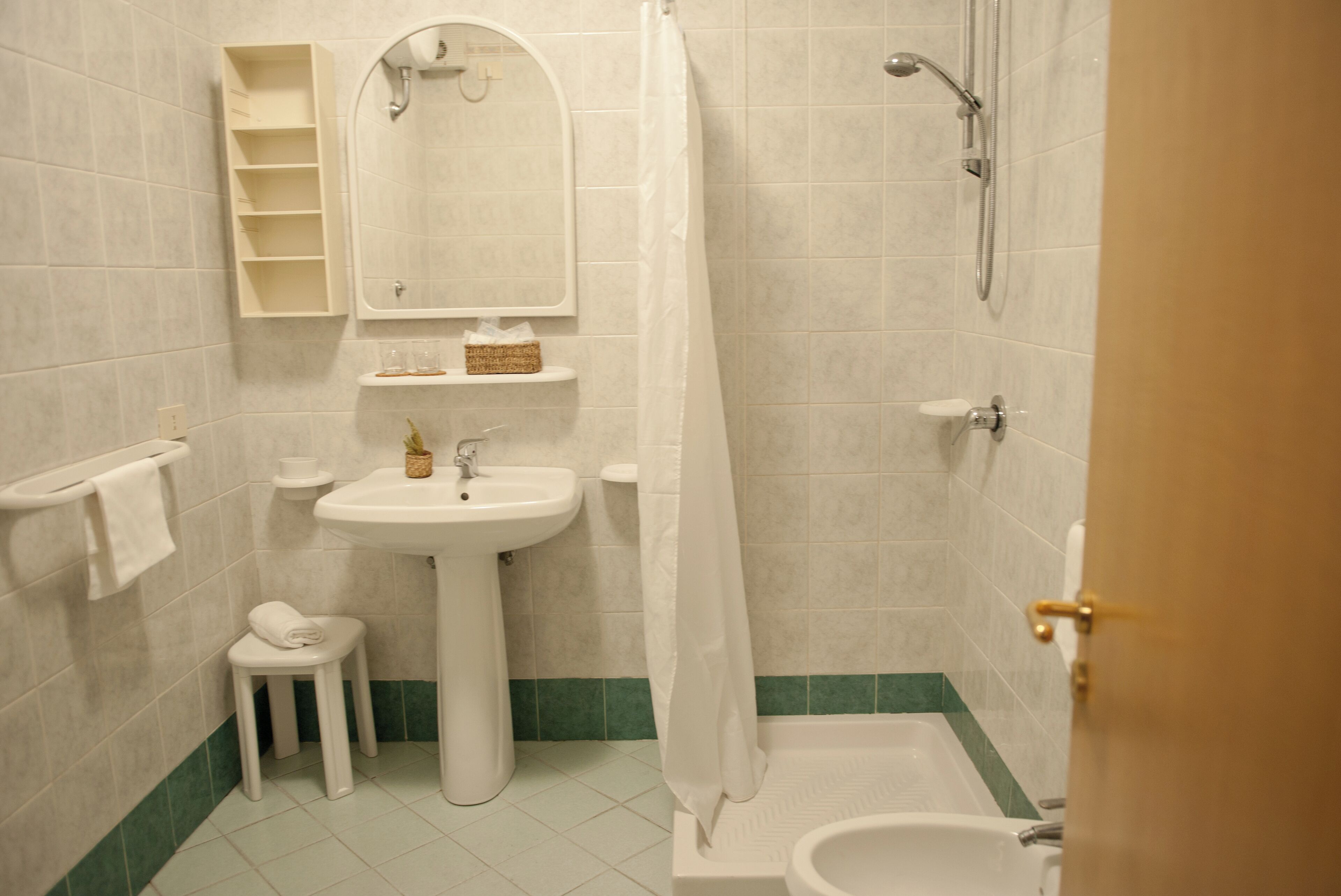 Casa de banho com lavatório suspenso, um banquinho pequeno, chuveiro com cortina e banheira.