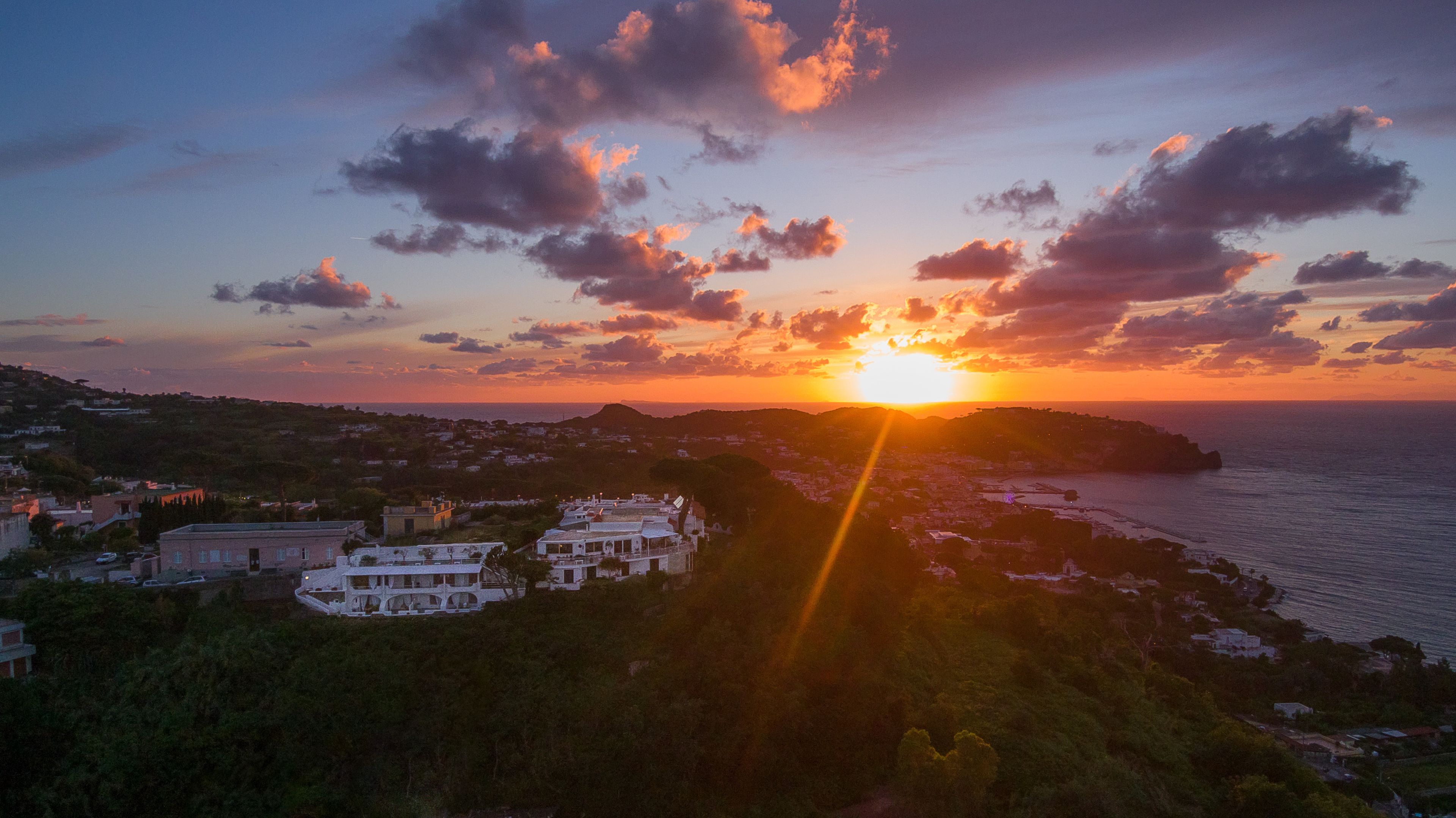A coastal landscape with a sunset, buildings, and a view of the sea.