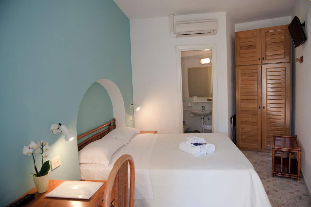 A neatly arranged bedroom with a bed, bedside table, lamp, and a potted plant.