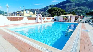 A rectangular swimming pool with clear blue water, surrounded by a tiled deck and a white wall with decorative cutouts.