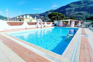 Una piscina rectangular con agua azul cristalina, rodeada por un solárium de baldosas y una pared blanca con detalles decorativos.