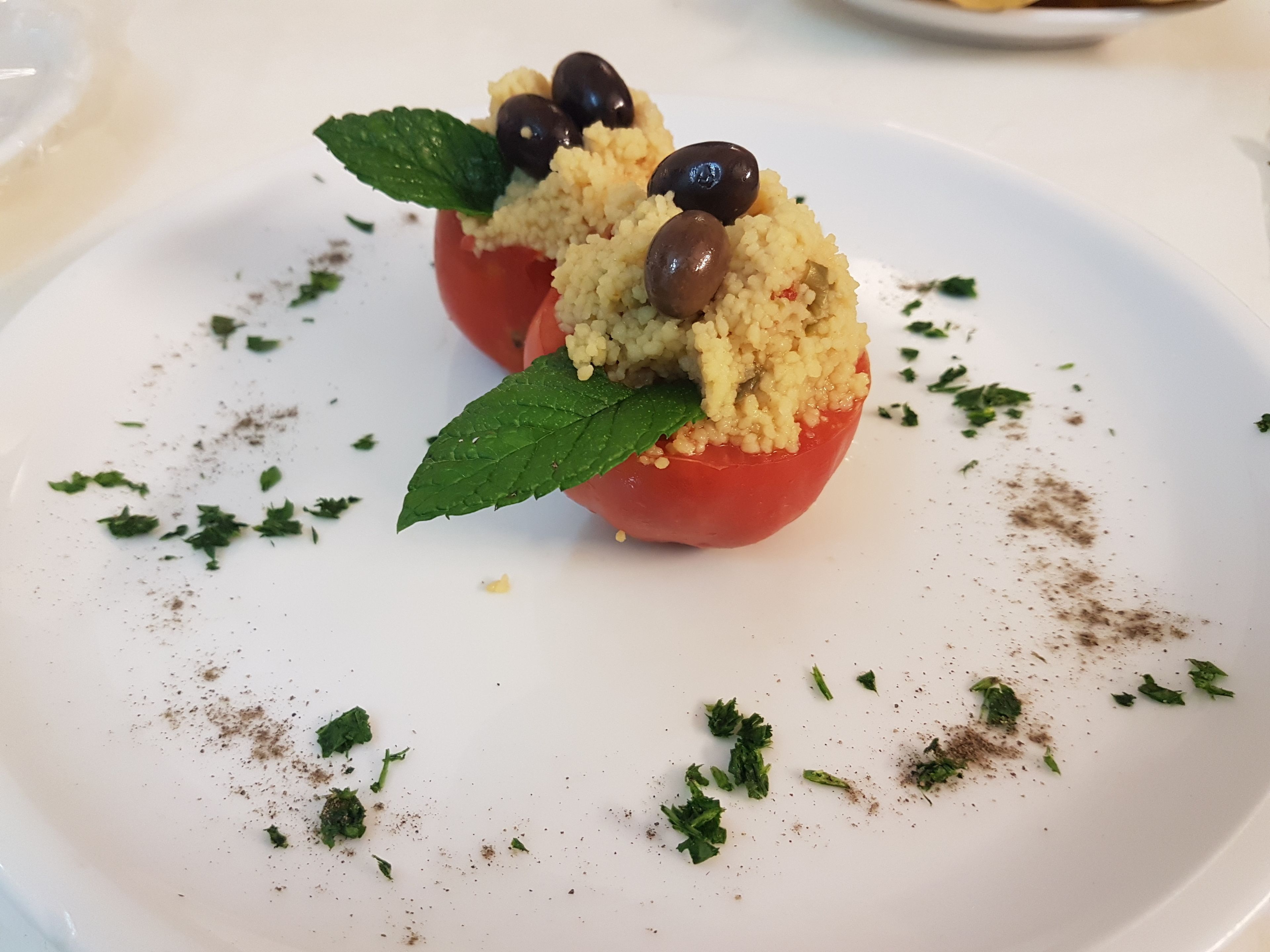 Une assiette contenant deux tomates farcies, garnies d’huile d’olive, d’herbes et d’épices.