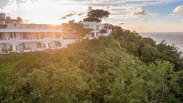 Un edificio costero con varios balcones que dan al mar, rodeado de exuberante vegetación.