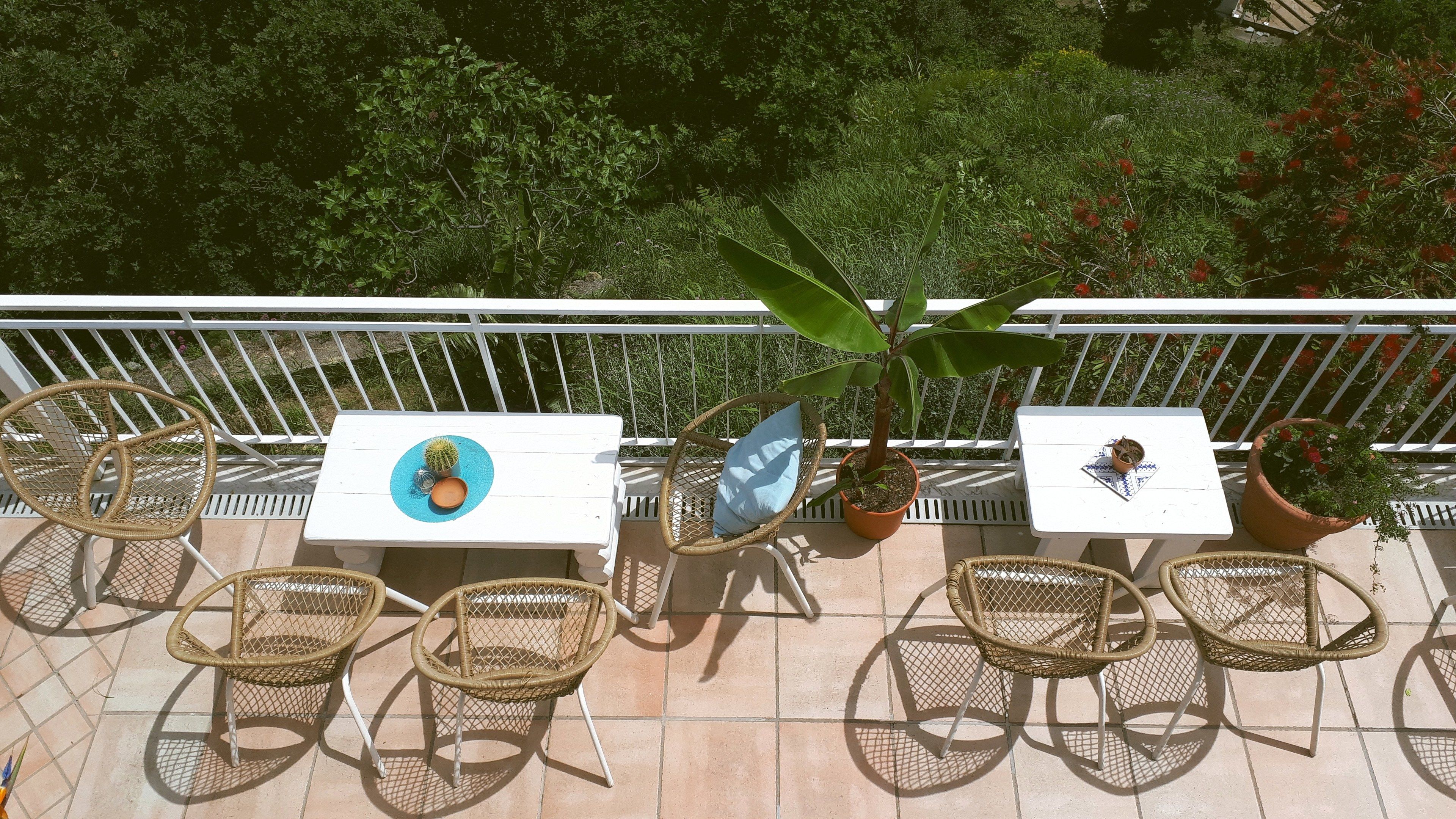 An outdoor patio with two white tables, wicker chairs, and potted plants.