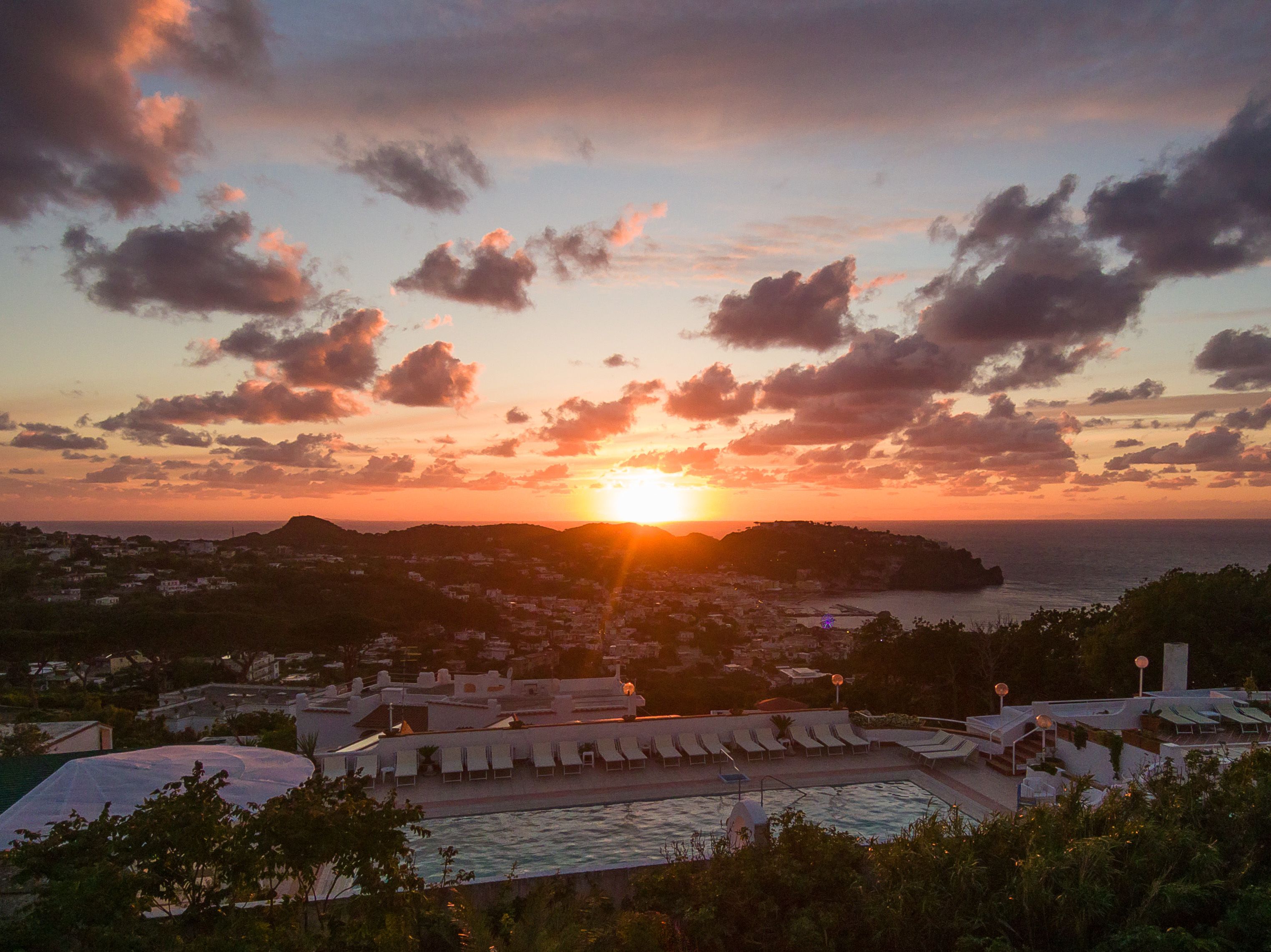 Un resort con piscina, aree prendisole e vista sul tramonto sull'oceano.