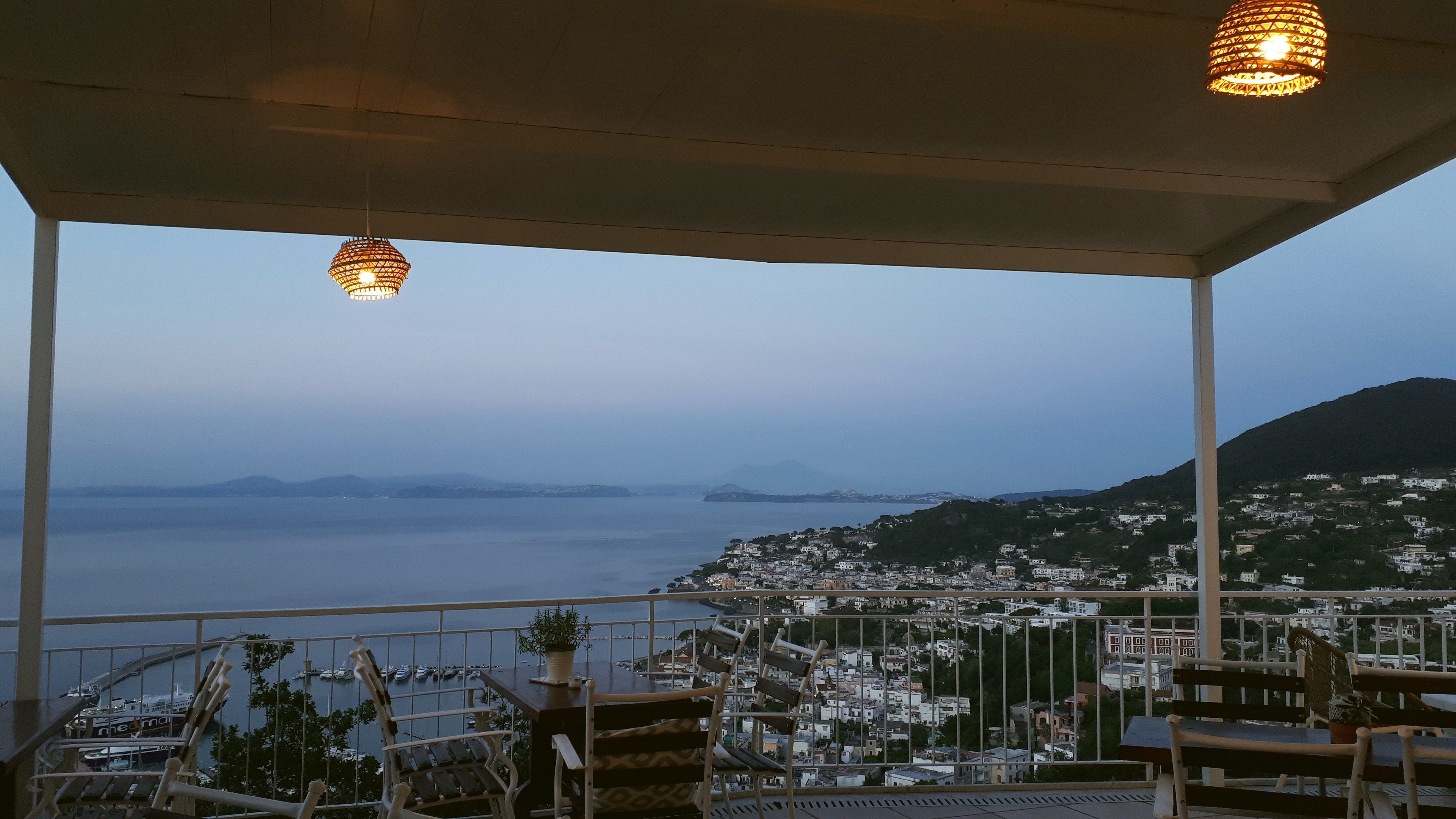 A balcony with a view of a coastal town, a body of water, and distant mountains.