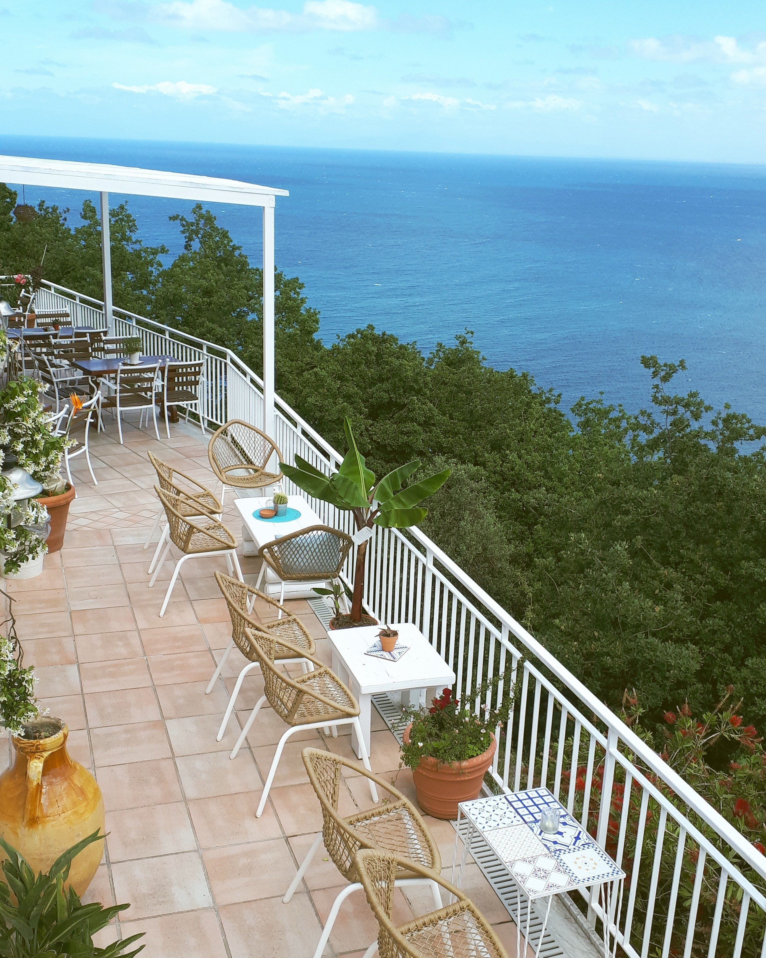 A terrace with wicker chairs and tables, overlooking the sea.