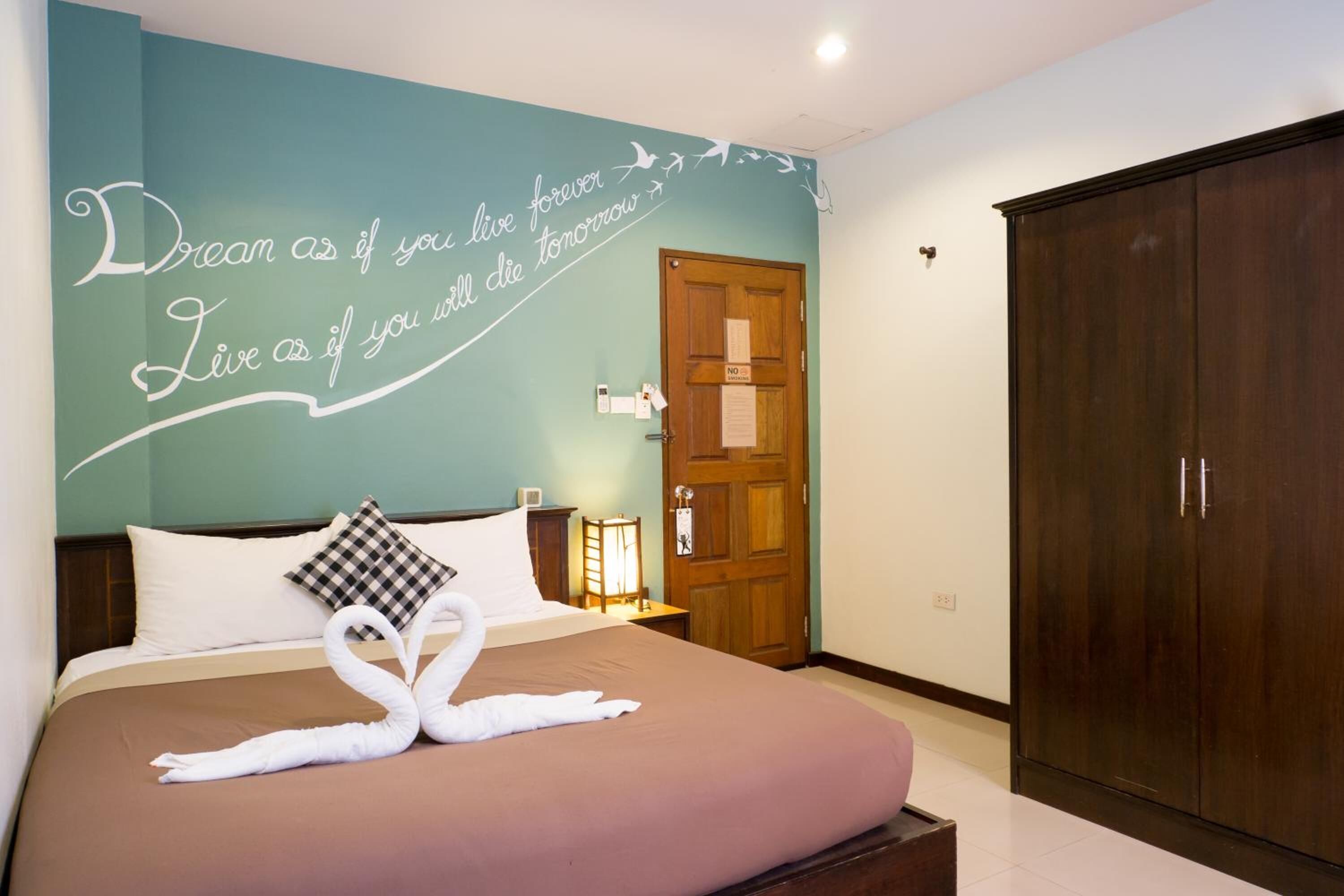Une chambre d’hôtel avec un lit, un mur orné d’inscriptions motivantes, une armoire et une porte sur laquelle est apposée une pancarte « DÉFENSE D’ENTRER ».