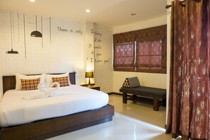 A hotel room with a large bed, a wall-mounted light fixture, a bench, and a window with curtains. - Bt Inn Patong (Patong)